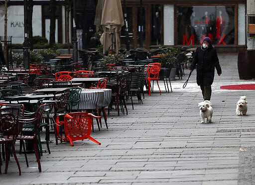 A woman walks with dogs in a deserted street amid the coronavirus outbreak in downtown Belgrade, Serbia, Thursday, March 26, 2020.   (AP Photo/Darko Vojinovic)