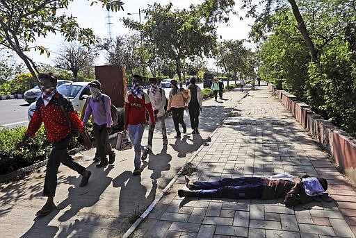 A homeless person sleeps by the side of a road as migrant daily wage laborers make the journey to their respective villages on foot following a lockdown amid concern over spread of coronavirus in New Delhi, India, Friday, March 27, 2020. Some of India's legions of poor and others suddenly thrown out of work by a nationwide stay-at-home order began receiving aid on Thursday, as both public and private groups worked to blunt the impact of efforts to curb the coronavirus pandemic. The measures that went into effect Wednesday, the largest of their kind in the world, risk heaping further hardship on the quarter of the population who live below the poverty line and the 1.8 million who are homeless. (AP Photo/Manish Swarup)