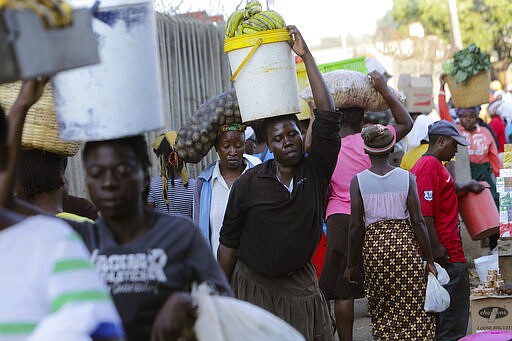 Women carry food at a local market in Harare, Zimbabwe, Friday, March 27, 2020. Zimbabwe's public hospital doctors are on strike over what they called a lack of adequate protective gear as the coronavirus begins to spread in a country whose health system has almost collapsed. The new coronavirus causes mild or moderate symptoms for most people, but for some, especially older adults and people with existing health problems, it can cause more severe illness or death. (AP Photo/Tsvangirayi Mukwazhi)