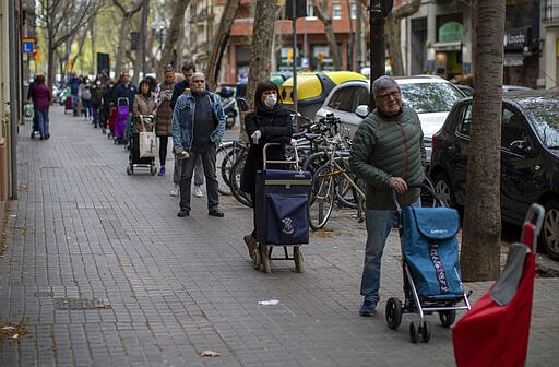 People line up to buy supplies from a shop during the coronavirus outbreak in Barcelona, Spain, Friday, March 27, 2020. The new coronavirus causes mild or moderate symptoms for most people, but for some, especially older adults and people with existing health problems, it can cause more severe illness or death. (AP Photo/Emilio Morenatti)