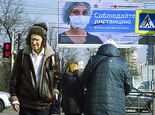 People walk past an electronic billboard showing a doctor wearing a medical mask with the words reading &quot;Keep distance with other people, it will save a life&quot; in a street in St.Petersburg, Russia, Friday, March 27, 2020. The new coronavirus causes mild or moderate symptoms for most people, but for some, especially older adults and people with existing health problems, it can cause more severe illness or death. (AP Photo/Dmitri Lovetsky)