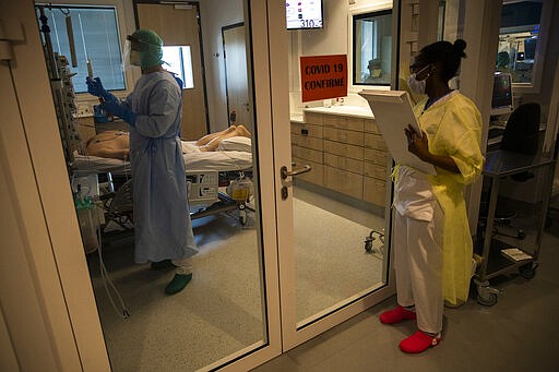 In this photograph taken from behind a window medical personnel work in the intensive care ward for Covid-19 patients at the MontLegia CHC hospital in Liege, Belgium, Friday, March 27, 2020. The new coronavirus causes mild or moderate symptoms for most people, but for some, especially older adults and people with existing health problems, it can cause more severe illness or death. (AP Photo/Francisco Seco)