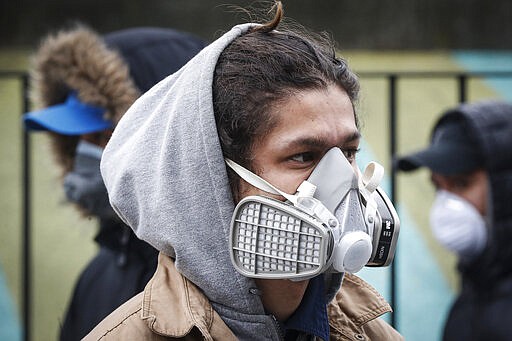 FILE - In this Wednesday, March 25, 2020, file photo, a person wears protective equipment while waiting to enter a COVID-19 testing site at Elmhurst Hospital Center in the Queens borough of New York. Los Angeles is half the size of New York City but has a disproportionately small fraction of the coronavirus cases and deaths as the nation's largest city. The same goes for California when compared with New York state as a whole, which is the current epicenter of the outbreak in the U.S. Public health officials in Los Angeles are bracing for the worst yet to come and warning that the city and county of Los Angeles could see as devastating an impact as New York in coming days. (AP Photo/John Minchillo, File)