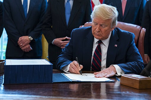 President Donald Trump signs the coronavirus stimulus relief package in the Oval Office at the White House, Friday, March 27, 2020, in Washington. (AP Photo/Evan Vucci)