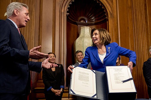 House Speaker Nancy Pelosi of Calif., right, speaks with House Minority Leader Kevin McCarthy of Calif., left, as she holds up the Coronavirus Aid, Relief, and Economic Security (CARES) Act after signing it on Capitol Hill, Friday, March 27, 2020, in Washington. The $2.2 trillion package will head to head to President Donald Trump for his signature. (AP Photo/Andrew Harnik)