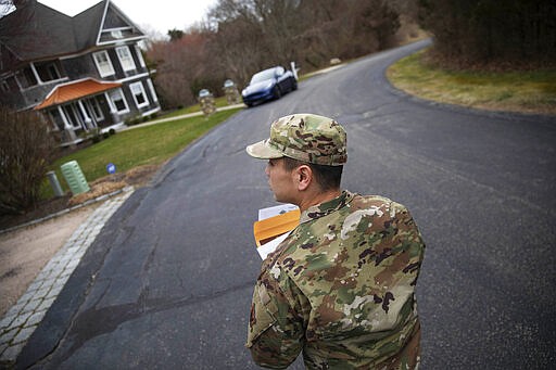 Rhode Island Air National Guard Tsgt. William Randall walks through the Watch Hill neighborhood looking for New York residents to inform them of self quarantine orders, Saturday, March 28, 2020, in Westerly, R.I. States are pulling back the welcome mat for travelers from the New York area, which is the epicenter of the country's coronavirus outbreak, and some say at least one state's measures are unconstitutional. Gov. Gina Raimondo ratcheted up the measures announcing she ordered the state National Guard to go door-to-door in coastal communities starting this weekend to find out whether any of the home's residents have recently arrived from New York and inform them of the quarantine order. (AP Photo/David Goldman)