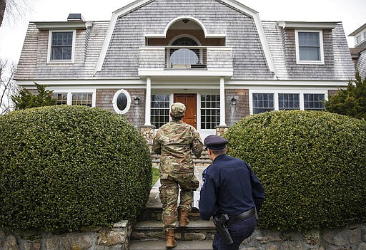 Rhode Island Air National Guard Tsgt. William Randall, left, and Westerly police officer Howard Mills approach a home while looking for New York license plates in driveways to inform them of self quarantine orders, Saturday, March 28, 2020, in Westerly, R.I. States are pulling back the welcome mat for travelers from the New York area, which is the epicenter of the country's coronavirus outbreak, and some say at least one state's measures are unconstitutional. Gov. Gina Raimondo ratcheted up the measures announcing she ordered the state National Guard to go door-to-door in coastal communities starting this weekend to find out whether any of the home's residents have recently arrived from New York and inform them of the quarantine order. (AP Photo/David Goldman)