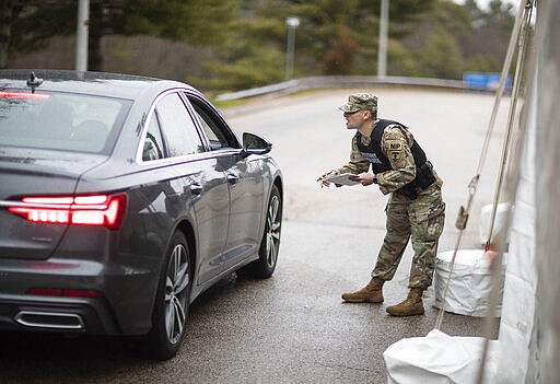 A member of the Rhode Island National Guard Military Police talks with a motorist with New York license plates at a checkpoint on I-95 near the border with Connecticut where New Yorkers must pull over and provide contact information and are told to self-quarantine for two weeks, Saturday, March 28, 2020, in Hope Valley, R.I. Rhode Island Gov. Gina Raimondo on Saturday ordered anyone visiting the state to self-quarantine for 14 days and restricted residents to stay at home and nonessential retail businesses to close Monday until April 13 to help stop the spread of the coronavirus. (AP Photo/David Goldman)