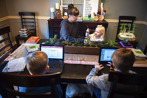 Emily Williams, third-grade teacher of Austinville Elementary, left, helps her daughter Lily, 3, as her two sons Braden, 10, bottom left, and Landen, 8, complete school assigned virtual assignments on Friday, March 20, 2020, at their home in Decatur, Ala. (Dan Busey/The Decatur Daily via AP)