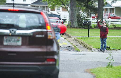 An Austinville Elementary School student waves at his teachers as they drive on a parade Wednesday, March 25, 2020 through the neighborhoods where their students live in Decatur, Ala. to show them their love and encourage them to keep studying, reading and learning while the school is closed due to the coronavirus pandemic. (Jeronimo Nisa/The Decatur Daily via AP)