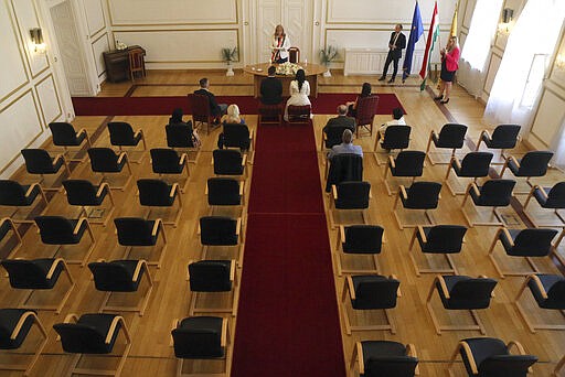 Groom Gyorgy David Jablonovszky and his bride Timea Jablonovszky attend their wedding ceremony along with their family members at the town hall of Miskolc, Hungary, Saturday, March 28, 2020. The couple celebrate today without wedding guests because of the government regulations to prevent the COVID-19 coronavirus pandemic. The new coronavirus causes mild or moderate symptoms for most people, but for some, especially older adults and people with existing health problems, it can cause more severe illness or death. (Janos Vajda/MTI via AP)