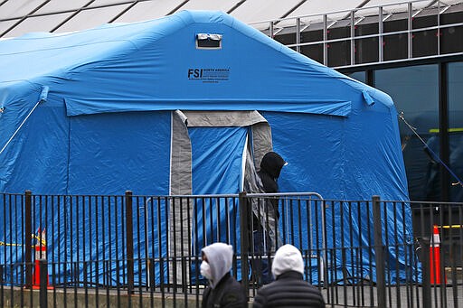 A person emerges from a tent set up in the driveway of the emergency entrance to Elmhurst Hospital Center in New York, Saturday, March 28, 2020, as others wait in line to be tested for coronavirus. The hospital is caring for a high number of coronavirus patients in the city.  (AP Photo/Kathy Willens)