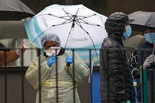 A medical worker points out the COVID-19 testing tent set up outside Elmhurst Hospital Center in New York, Saturday, March 28, 2020. The hospital is caring for a high number of coronavirus patients in the city.  The new coronavirus causes mild or moderate symptoms for most people, but for some, especially older adults and people with existing health problems, it can cause more severe illness or death. (AP Photo/Kathy Willens)