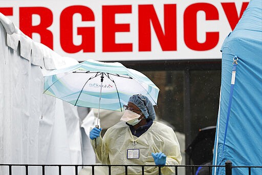 A medical worker holds an umbrella as she checks to to see if anyone is waiting in line outside a COVID-19 testing center at Elmhurst Hospital Center in New York, Saturday, March 28, 2020. The hospital is caring for a high number of coronavirus patients. (AP Photo/Kathy Willens)