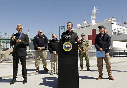 California Governor Gavin Newsom speaks in front of the hospital ship US Naval Ship Mercy that arrived into the Port of Los Angeles on Friday, March 27, 2020, to provide relief for Southland hospitals overwhelmed by the coronavirus pandemic. Also attending the press conference and keeping appropriate distancing are Los Angeles Mayor Eric Garcetti, right, Dr. Mark Ghaly, Secretary of Health and Human Services, behind Garcetti, Director Mark Ghilarducci, Cal OES, third left, Robert Fenton, FEMA Regional Administrator for Region 9, second left, U.S. Navy Admiral John Gumbleton, third right, and interpreter Richard Pope, left. (Carolyn Cole/Los Angeles Times via AP, Pool)