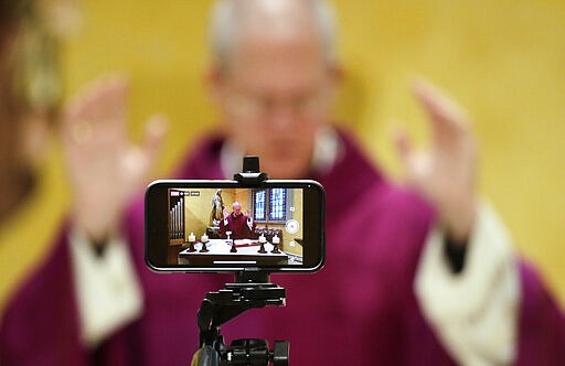 A cell phone is used to live stream mass by Archbishop Paul D. Etienne at St. James Cathedral, the Cathedral for the Catholic Archdiocese of Seattle, where open masses have been suspended because of the coronavirus outbreak, Saturday, March 28, 2020, in Seattle. The church remains open for people to sit in the sanctuary in the mornings and is live streaming a mass every morning. (AP Photo/Elaine Thompson)