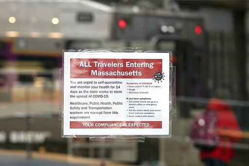 A sign posted in the Amtrak terminus at South Station in Boston, Saturday, March 28, 2020, urges travelers entering Massachusetts to self-quarantine for 14 days. The new coronavirus causes mild or moderate symptoms for most people, but for some, especially older adults and people with existing health problems, it can cause more severe illness or death. (AP Photo/Michael Dwyer)