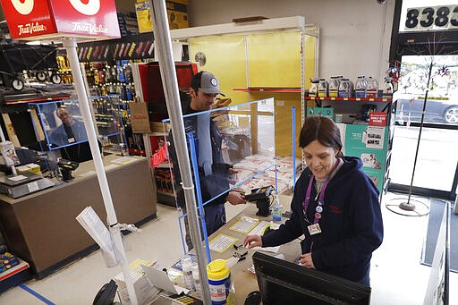 In this photo taken Wednesday, March 25, 2020, hardware clerk Rebecca Peil, right, works behind a plexiglass barrier built a few days earlier by a co-worker to help protect employees and customers during the coronavirus outbreak, in Seattle. The store is expected to remain open under Gov. Jay Inslee's stay-at-home order issued Monday in the midst of the coronavirus outbreak, with only &quot;essential&quot; service providers allowed to go to their jobs. (AP Photo/Elaine Thompson)