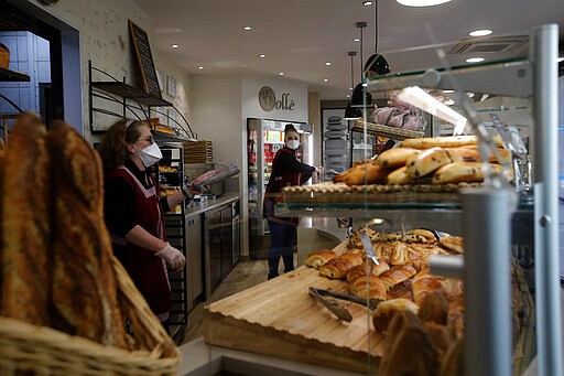 FILE - In this March 24, 2020, file photo, bakers sell bread in a Boulogne-Billancourt bakery outside Paris. The coronavirus pandemic has much of the world contemplating an existential question amid a growing number of stay-at-home orders, with only &quot;essential&quot; service providers allowed to go to their jobs. As U.S. states enact sweeping stay-at-home orders, there is lots of agreement on what's essential, but some have their own notions. A few are eyebrow raisers. Among them are guns, golf and cannabis. Most lists, being compiled by governors and others, capture the basics of what's essential. (AP Photo/Christophe Ena,File)