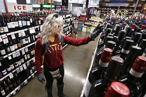 In this photo taken Wednesday, March 25, 2020, Lisa MacDonald shops for wine in a liquor store in Seattle. Many, if not most, liquor stores in Washington state are considered &quot;essential businesses&quot; and can stay open under Gov. Jay Inslee's stay-at-home order issued Monday in the midst of the coronavirus outbreak. (AP Photo/Elaine Thompson)