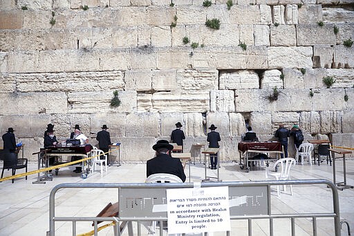 FILE - In this March 15, 2020, file photo Ultra Orthodox Jews practicing social distancing pray at the Western Wall in Jerusalem. The coronavirus pandemic has much of the world contemplating an existential question amid a growing number of stay-at-home orders, with only &quot;essential&quot; service providers allowed to go to their jobs. As U.S. states enact sweeping stay-at-home orders, there is lots of agreement on what's essential, but some have their own notions. A few are eyebrow raisers. Among them are guns, golf and cannabis. Most lists, being compiled by governors and others, capture the basics of what's essential. (AP Photo/Mahmoud Illean, File)