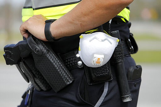 A North Charleston police officer carries a protective mask around his gun belt while working traffic at Roper St. Francis' North Charleston office Monday, March 16, 2020, in North Charleston, S.C. Roper St. Francis Healthcare is providing drive-thru specimen collecting for patients suspected of having COVID-19 or flu who have already been screened by a virtual care provider. (AP Photo/Mic Smith)