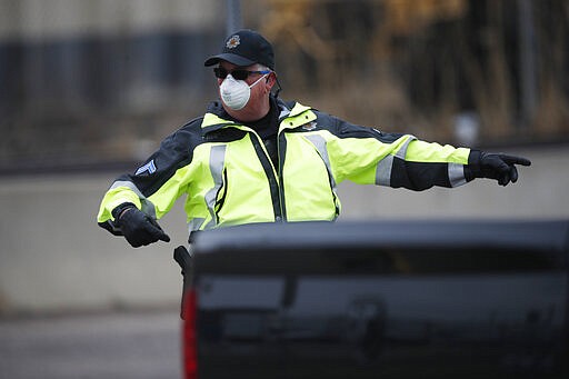 A Denver Police Department officer wears a surgical mask while directing traffic at a coronavirus drive-thru testing site outside the Denver Coliseum Saturday, March 14, 2020, in Denver. Officials planned to administer 150 tests but the line of vehicles wrapped around three city blocks. (AP Photo/David Zalubowski)