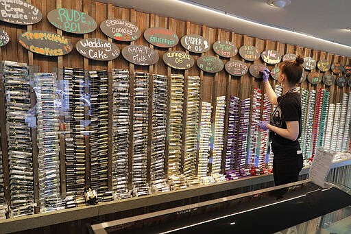 In this photo taken March 24, 2020, budtender Maegan Clark writes on a sign at the pre-roll area of The Reef Capitol Hill, a marijuana store in Seattle. Earlier in the week, Washington Gov. Jay Inslee ordered nonessential businesses to close and the state's more than 7 million residents to stay home in order to slow the spread of the new coronavirus. In Washington and several other states where marijuana is legal, pot shops and workers in the market's supply chain were deemed essential and allowed to remain open. Signs posted at the store said that The Reef is donating 5% of its profits to Seattle-area coronavirus relief efforts. (AP Photo/Ted S. Warren)