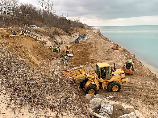 In this Jan. 2020 photo provided by Geof Benson, crews use bulldozers to move sand along Lake Michigan's shoreline in Beverly Shores, Ind., in  to protect local beaches from storms that have scoured the region's shoreline during a period of near record high water levels. Leaders of several of Indiana's lakeside communities, including Beverly Shores, have urged Gov. Eric Holcomb to declare a state of emergency and help with funding to fight erosion that's eating away at beaches important to local tourism and threatening beachside homes. (Courtesy of Geof Benson via AP)