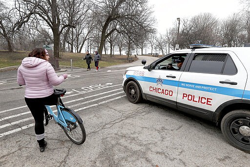 FILE - In this March 26, 2020, file photo, a Chicago police officer notifies a cyclist that the trails in Promontory Park, along Lake Michigan, are closed in an effort to limit the spread of COVID-19 infections, in Chicago. Chicago Mayor Lori Lightfoot's decision to shut down the trails along Lake Michigan and nearby parks during the coronavirus crisis underscores a growing concern that the large crowds of people flocking to beaches, parks and playgrounds are making it easier for the virus to spread.  (AP Photo/Charles Rex Arbogast, File)