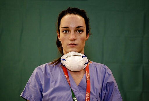 Martina Papponetti, 25, a nurse at the Humanitas Gavazzeni Hospital in Bergamo, Italy poses for a portrait at the end of her shift Friday, March 27, 2020. Their eyes are tired. Their cheekbones rubbed raw from protective masks. They don't smile. The doctors and nurses on the front lines of the coronavirus pandemic in Italy are almost unrecognizable behind their masks, scrubs, gloves and hairnets - the flimsy battle armor donned at the start of each shift as the only barrier to contagion. (AP Photo/Antonio Calanni)