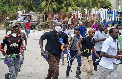 Ferry passengers flee from police firing tear gas, after new measures aimed at halting the spread of the new coronavirus instead caused a crowd to form outside the ferry in Mombasa, Kenya Friday, March 27, 2020. The new measures required public transport vehicles to drop passengers 1km away and walk to the ferry terminal and then queue, but passengers fearing they would get stuck before a 7pm curfew started crowding to get on causing police to fire tear gas and round up the passengers. (AP Photo)