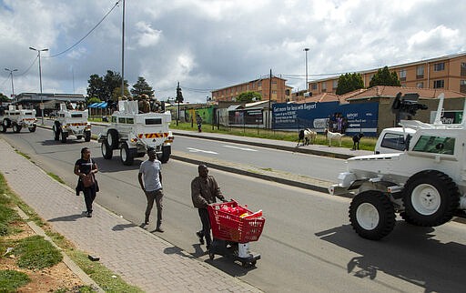 A man pushing a shopping cart with food on the street as South African National Defence Forces drive through a densely populated Alexandra township east of Johannesburg, South Africa, Saturday, March 28, 2020. South Africa went into a nationwide lockdown for 21 days in an effort to control the spread of the COVID-19 coronavirus. The new coronavirus causes mild or moderate symptoms for most people, but for some, especially older adults and people with existing health problems, it can cause more severe illness or death. (AP Photo/Themba Hadebe)