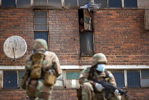 A hostel dweller watches on the South African National Defense Forces take positions ouside the hostel in a densely populated Alexandra township east of Johannesburg, South Africa, Saturday, March 28, 2020. South Africa went into a nationwide lockdown for 21 days in an effort to control the spread of the COVID-19 coronavirus. The new coronavirus causes mild or moderate symptoms for most people, but for some, especially older adults and people with existing health problems, it can cause more severe illness or death. (AP Photo/Themba Hadebe)