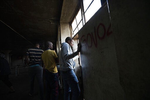 Residents of the Men's Hostel in the densely populated Alexandra township east of Johannesburg look at a deployment of South African National Defense Forces surrounding them Saturday, March 28, 2020. South Africa went into a nationwide lockdown for 21 days in an effort to control the spread of the COVID-19 coronavirus. The new coronavirus causes mild or moderate symptoms for most people, but for some, especially older adults and people with existing health problems, it can cause more severe illness or death. (AP Photo/Jerome Delay)