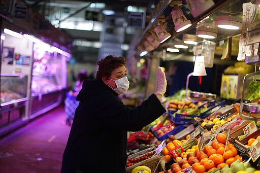 A woman wearing a face mask and gloves protection against coronavirus buys vegetables in a municipal market in Madrid, Spain, Saturday, March 28, 2020. The highly contagious CODIC-19 coronavirus has impacted on society around the globe, with many people self imposing isolation, and social distancing when they move from their homes. (AP Photo/Manu Fernandez)