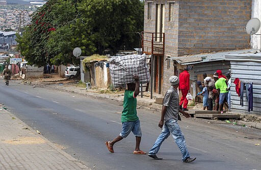 A man carrying a bag on his had crosses the street as the South African National Defence Forces patrol a densely populated Alexandra township east of Johannesburg, South Africa, Saturday, March 28, 2020. South Africa went into a nationwide lockdown for 21 days in an effort to control the spread of the COVID-19 coronavirus.  The new coronavirus causes mild or moderate symptoms for most people, but for some, especially older adults and people with existing health problems, it can cause more severe illness or death. (AP Photo/Themba Hadebe)