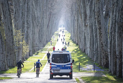 A police car drives through an avenue in the castle garden, which is more crowded on sunny days, Stuttgart, Germany, Saturday, March 29, 2020. To slow down the spread of the coronavirus, meetings of groups of more than two people are forbidden. Exceptions are families and persons living in the same household.(Sebastian Gollnow/dpa via AP)