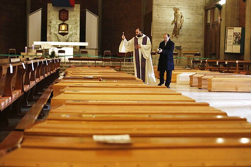 Don Marcello Crotti, left, blesses the coffins with Don Mario Carminati in the San Giuseppe church in Seriate, Italy, Saturday, March 28, 2020. The new coronavirus causes mild or moderate symptoms for most people, but for some, especially older adults and people with existing health problems, it can cause more severe illness or death. (AP Photo/Antonio Calanni)