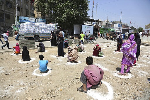 People sit at distance to receive relief goods during a nation-wide lockdown to contain outbreak of the coronavirus, in Karachi, Pakistan, Friday, March 27, 2020. The virus causes mild or moderate symptoms for most people, but for some, especially older adults and people with existing health problems, it can cause more severe illness or death. (AP Photo/Fareed Khan)