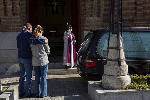 A priest wearing a face masks to protect against coronavirus performs funeral rites at a Madrid cemetery during the coronavirus outbreak in Madrid, Spain, Friday, March 27, 2020. The new coronavirus causes mild or moderate symptoms for most people, but for some, especially older adults and people with existing health problems, it can cause more severe illness or death. (AP Photo/Bernat Armangue)