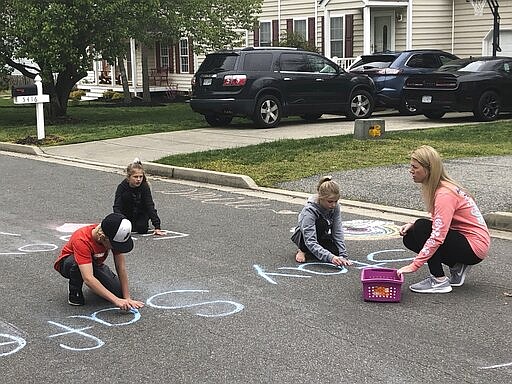 Jamie Burton, of Glen Allen, Va., and her three children, left to right, Carter, Cayden and Josie, write chalk messages to their neighbors as they stay at home during the coronavirus outbreak, Thursday, March 26, 2020. (AP Photo/Denise Lavoie)