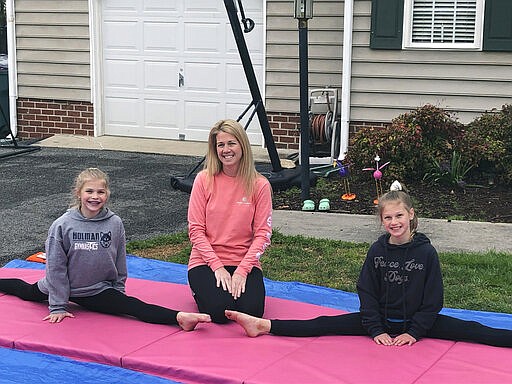 Jamie Burton, of Glen Allen, Va., and her two daughters, Josie, 12, left, and Cayden, 9, right, outside their home Thursday, March 26, 2020 on gymnastics mats. The Burtons have had more time together because the girls&#146; nightly gymnastics practices have been canceled because of the coronavirus outbreak. (AP Photo/Denise Lavoie)