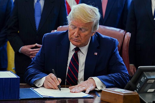 President Donald Trump signs the coronavirus stimulus relief package, in the Oval Office at the White House, Friday, March 27, 2020, in Washington. (AP Photo/Evan Vucci)