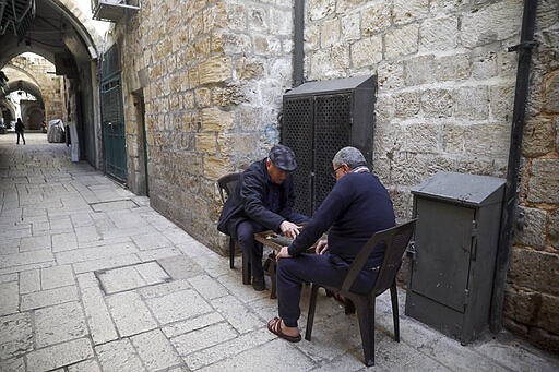 In this Thursday, March 26, 2020 photo, Palestinians play a board game in a deserted Old City in Jerusalem. As the coronavirus spreads across the Middle East, cherished traditions are coming to an abrupt halt: No more coffee shops where men gather to play cards and backgammon. (AP Photo/Mahmoud Illean)