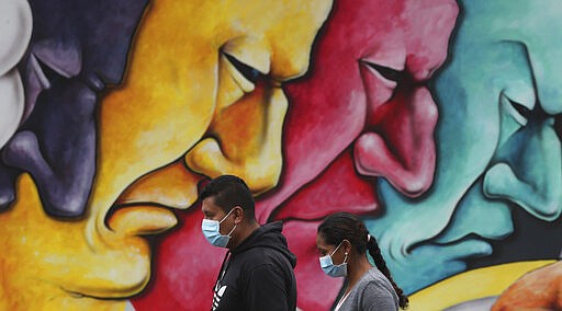 Pedestrians, wearing protective face masks as a precaution against the spread of the new coronavirus, walk past a mural in Quito, Ecuador, Saturday, March 28, 2020. The government has declared a health emergency, enacting a curfew and restricting movement to only those who provide basic services. (AP Photo/Dolores Ochoa)