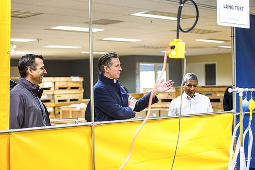 San Jose Mayor Sam Liccardo, left, and California Gov. Gavin Newsom, center, are given a tour of the Bloom Energy Sunnyvale, Calif., campus Saturday, March 28, 2020. Bloom Energy is a fuel cell generator company that has switched over to refurbishing ventilators as an increasing number of patients experience respiratory issues as a result of COVID-19. (Beth LaBerge/KQED via AP, Pool)