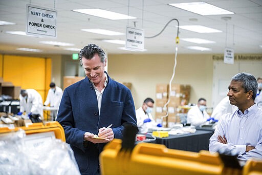 Bloom Energy CEO KR Sridhar, right, watches as California Gov. Gavin Newsom writes down a note during a tour with Sridhar of the Bloom Energy Sunnyvale campus, Saturday, March 28, 2020. Bloom Energy is a fuel cell generator company that has switched over to refurbishing ventilators as an increasing number of patients experience respiratory issues as a result of COVID-19. (Beth LaBerge/Pool Photo via AP)