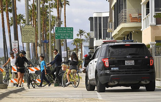 Los Angeles police officers shoo people away from the boardwalk at Venice Beach, Saturday, March 28, 2020, in Los Angeles. With cases of coronavirus surging and the death toll surpassing 100, lawmakers are pleading with cooped-up Californians to spend a second weekend at home to slow the spread of the infections. It has been more than a week since Gov. Gavin Newsom barred 40 million residents from going outdoors except for essentials. Even so, reports of crowds have prompted local and state officials to warn that ignoring social distancing, park and beach closures could spread the virus, which already is surging. (AP Photo/Mark J. Terrill)