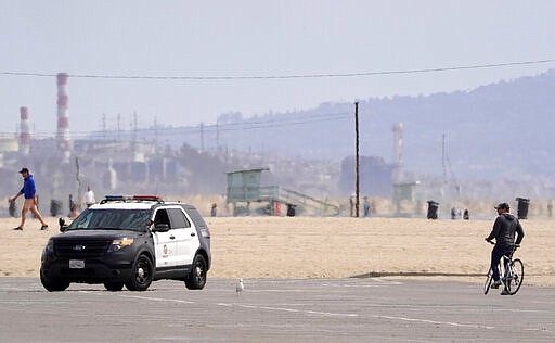 Los Angeles police officers patrol an empty parking lot at Venice Beach, Saturday, March 28, 2020, in Los Angeles. With cases of coronavirus surging and the death toll surpassing 100, lawmakers are pleading with cooped-up Californians to spend a second weekend at home to slow the spread of the infections. (AP Photo/Mark J. Terrill)